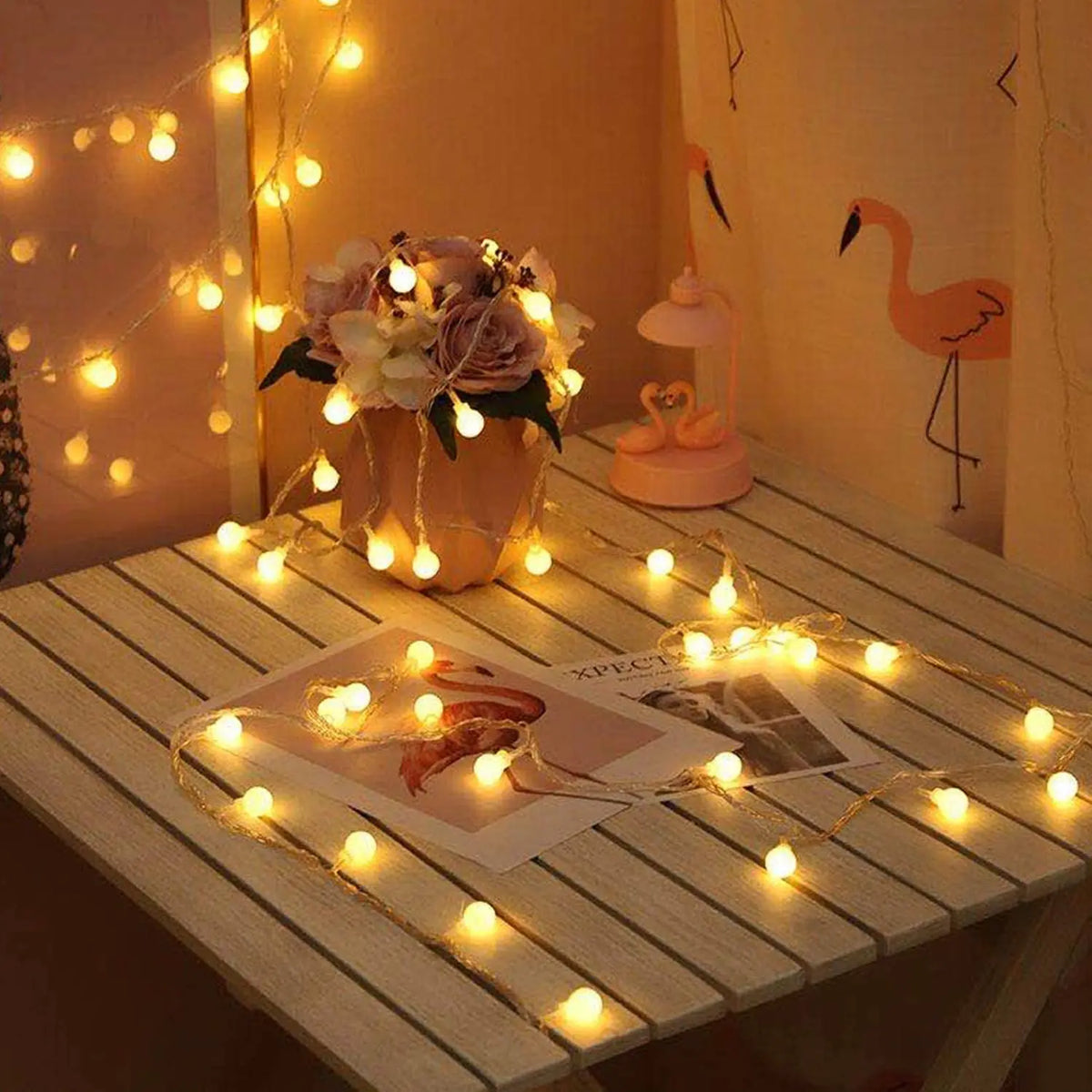 A close-up of battery-powered globe string lights illuminating a table with flowers and a decorative giraffe figurine.