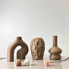 A set of three textured, earthy-toned geometric vases displayed on a white surface.