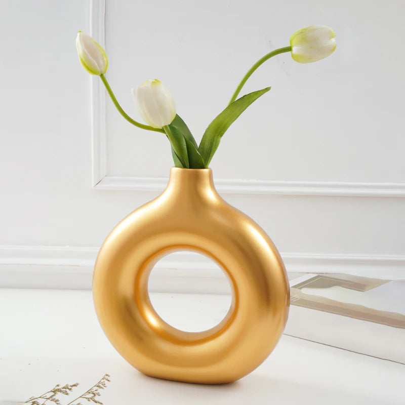 A golden, ring-shaped vase holds a stem of white tulips against a white background.