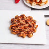 A golden waffle drizzled with syrup and topped with chopped nuts on a white plate.