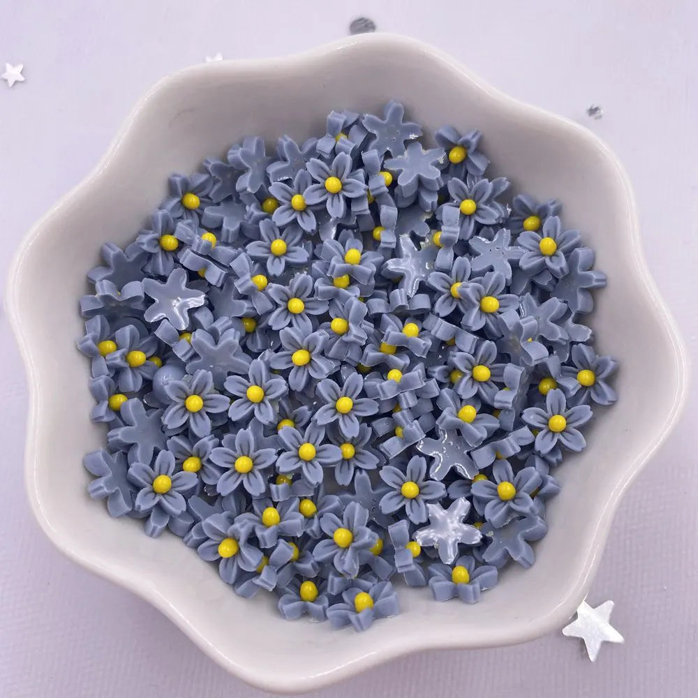 A pile of small, gray resin flower gems with yellow centers in a white dish.