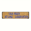 A wooden sign with blue text that reads Talk Much Sit Long Laugh Often