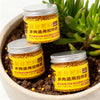 Two glass jars of granular slow-release plant fertilizer with yellow pellets are shown in a pot surrounded by green foliage.