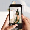 A hand holds a black smartphone displaying a photo of a woman with a ghost-like decoration on top.