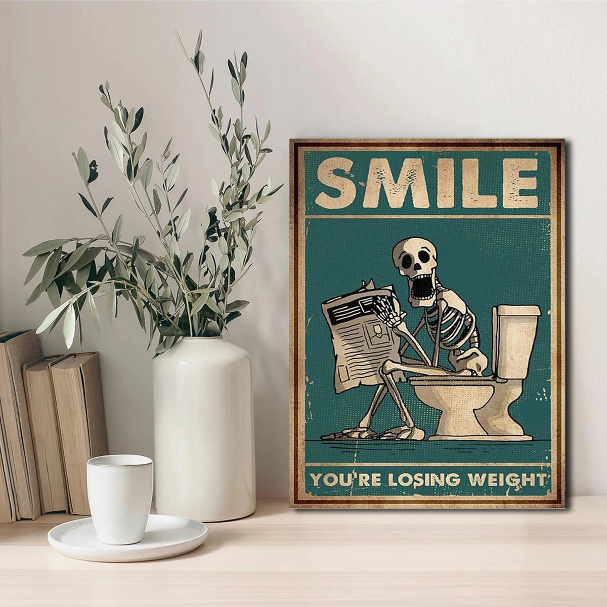 A canvas print featuring a skeleton man squatting on a toilet with the text You're losing weight.