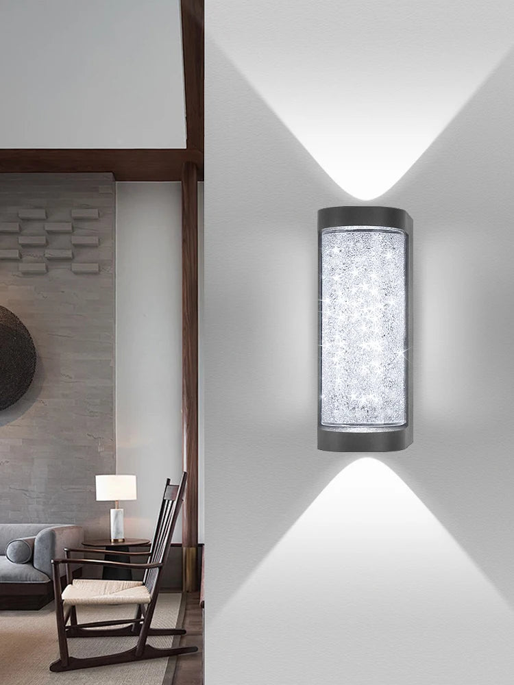 A modern LED crystal outdoor wall sconce mounted on a white wall, casting a bright light.