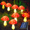Six glowing red and white spotted mushroom lights are displayed in a dark garden setting next to a solar panel.
