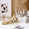Retro gold and silver foil resin letters spelling LOVE displayed on a white surface.