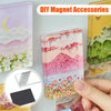 A hand holds a pink and purple acrylic photo magnet with a mountain landscape design.