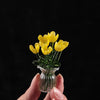 A hand holds a small glass vase filled with bright yellow handmade flowers for home decor.