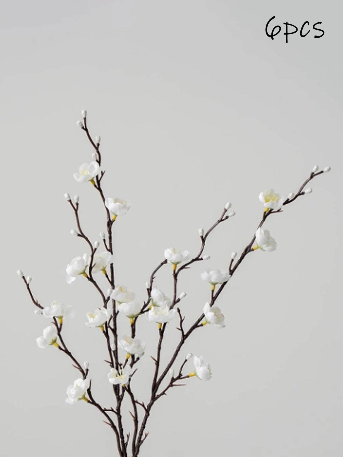 Una rama de flores blancas artificiales de ciruelo sobre un tallo oscuro contra un fondo gris claro.