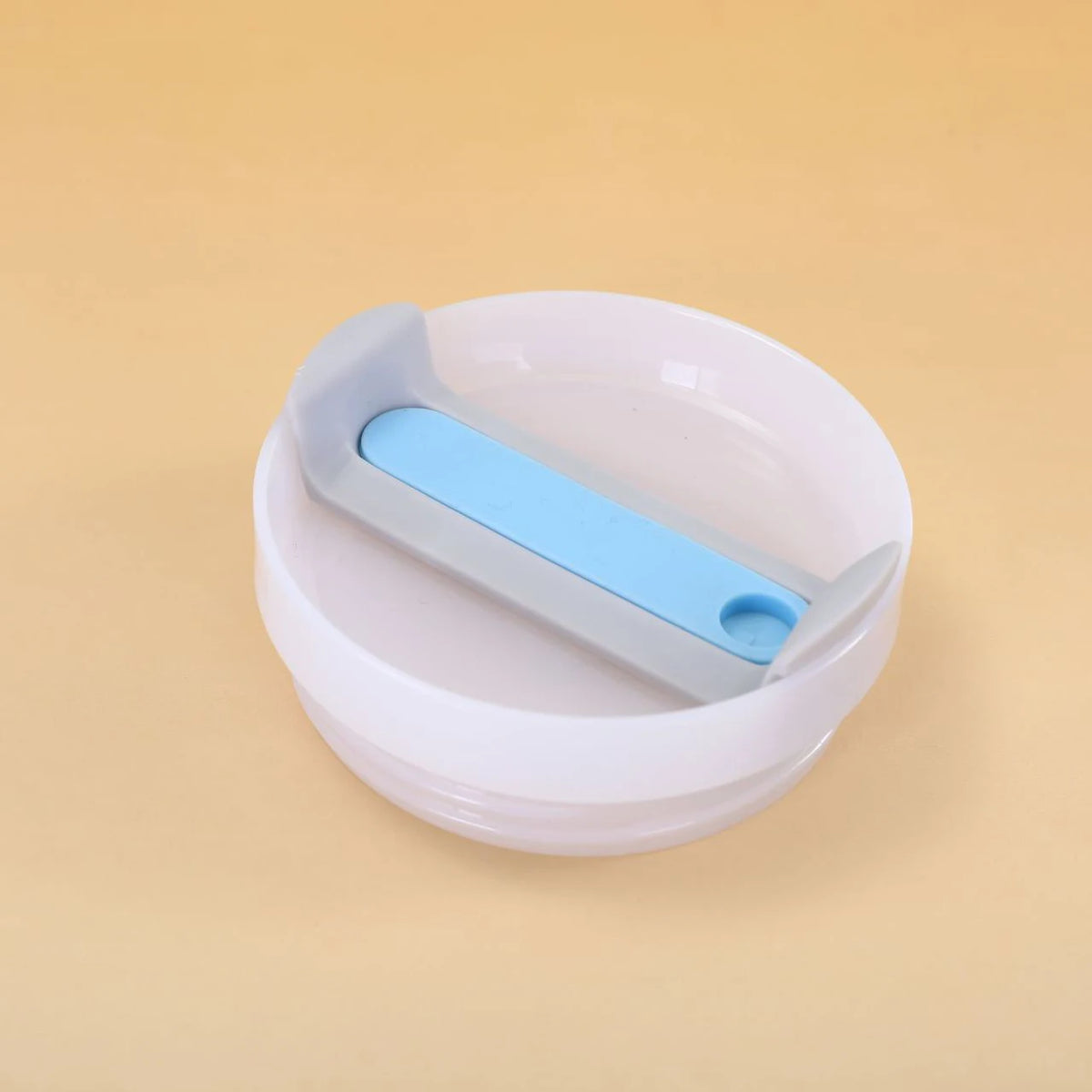 A white replacement tumbler lid with a light blue silicone cover is shown on a beige background.