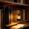 A black wrought iron lamp with a glass shade sits on a wooden shelf among old books.