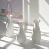 Three white ceramic bud vases with ribbed texture casting shadows on a light surface.