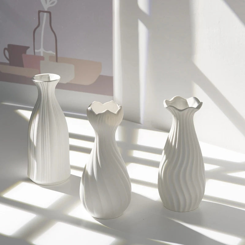 Three white ceramic bud vases with ribbed texture casting shadows on a light surface.