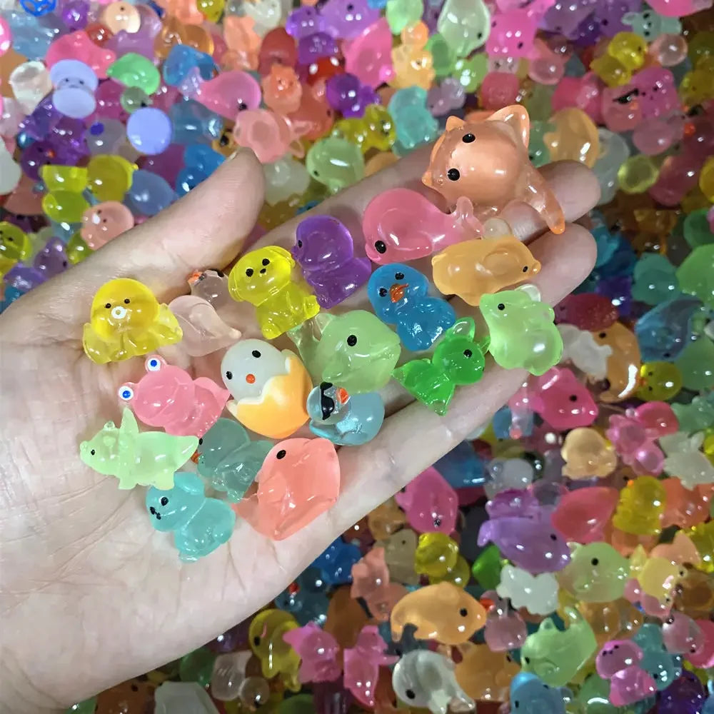 A hand holds a collection of colorful luminous resin animal figurines for aquarium decor.