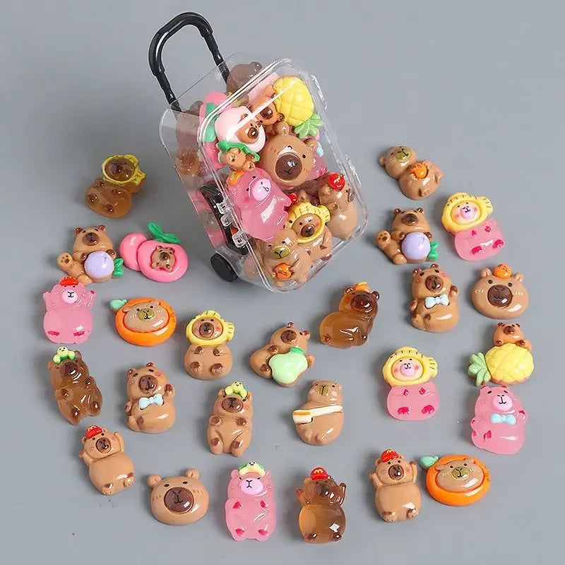 A collection of small capybara figures in various colors and textures, including a clear plastic suitcase.