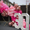 A pink and rose gold balloon garland celebrating a birthday, featuring balloons in various shades of pink and metallic rose g