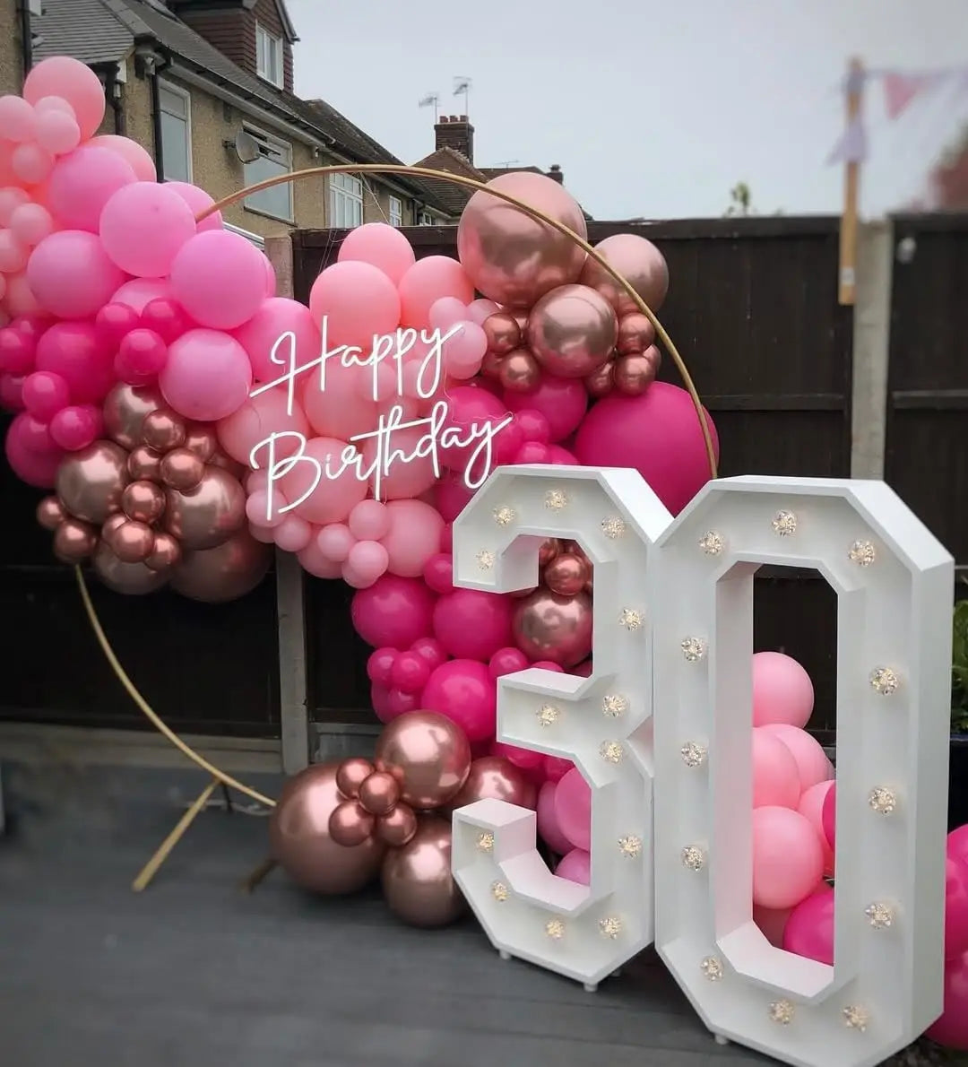 A pink and rose gold balloon garland celebrating a birthday, featuring balloons in various shades of pink and metallic rose g