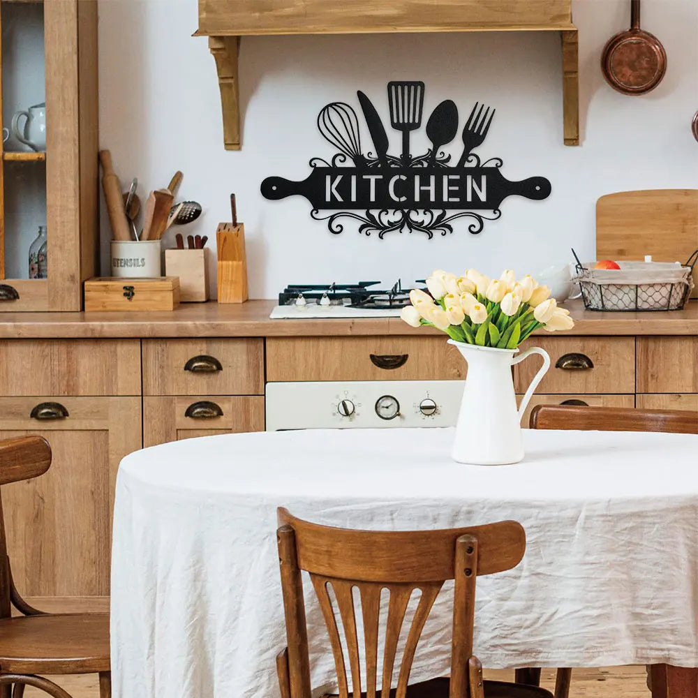 A rustic farmhouse metal wall sign featuring a silhouette of kitchen utensils above wooden cabinetry and a dining table.