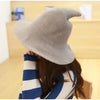 A person is wearing a beige vintage knit witch hat while looking down at it.