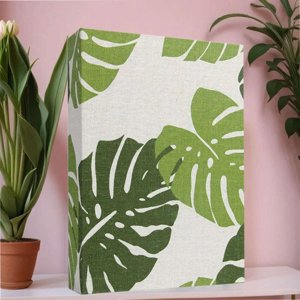 Vertikaler Fotobuch-Cover mit tropischem Monstera-Blattmuster auf weißem Leinenhintergrund.