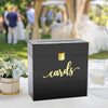 A black acrylic gift box with gold lettering labeled cards sits on a white surface in an outdoor event setting.