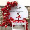 A red and gold balloon arch decoration featuring a white cake display against a stone wall.