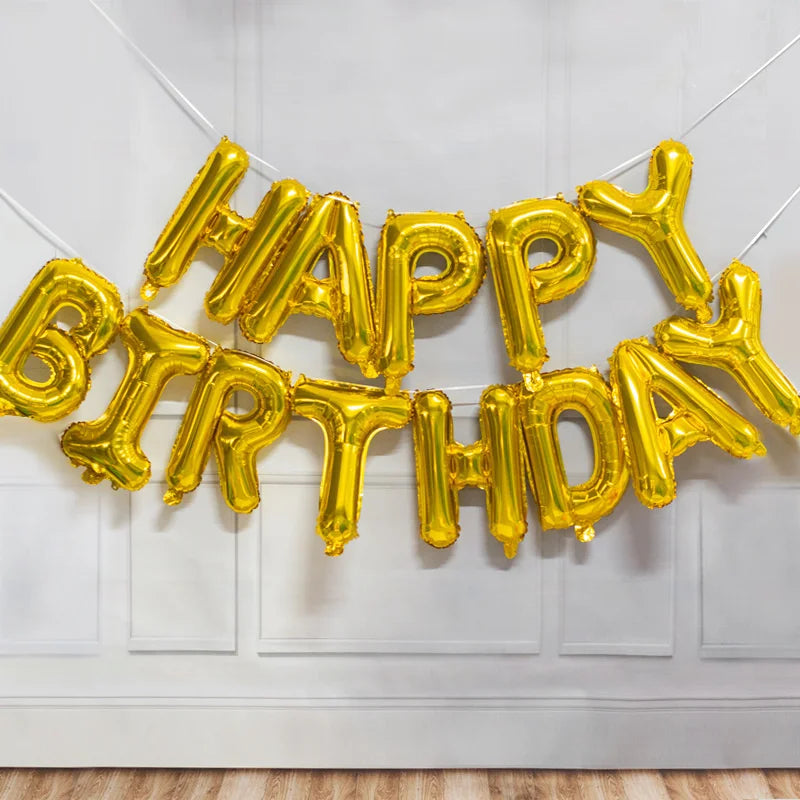 A golden foil letter balloon banner spelling out Happy Birthday hanging against a white wall.