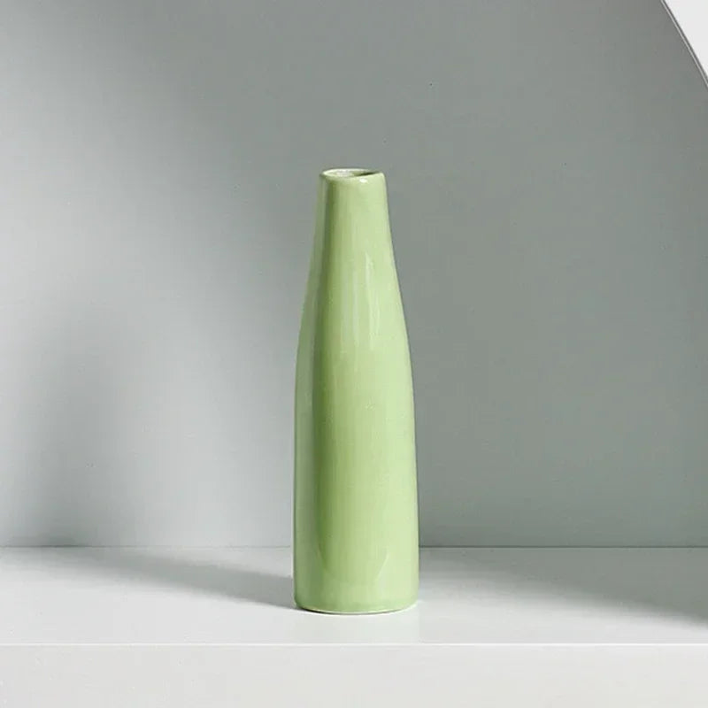A tall, slender light green ceramic vase standing on a white shelf.