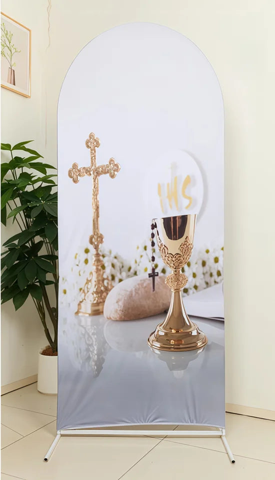 A gold-toned cross and a goblet are displayed on a silver backdrop for a party photo booth.