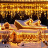 Warm yellow string lights drape over a snowy roof and house facade in a festive outdoor Christmas display.