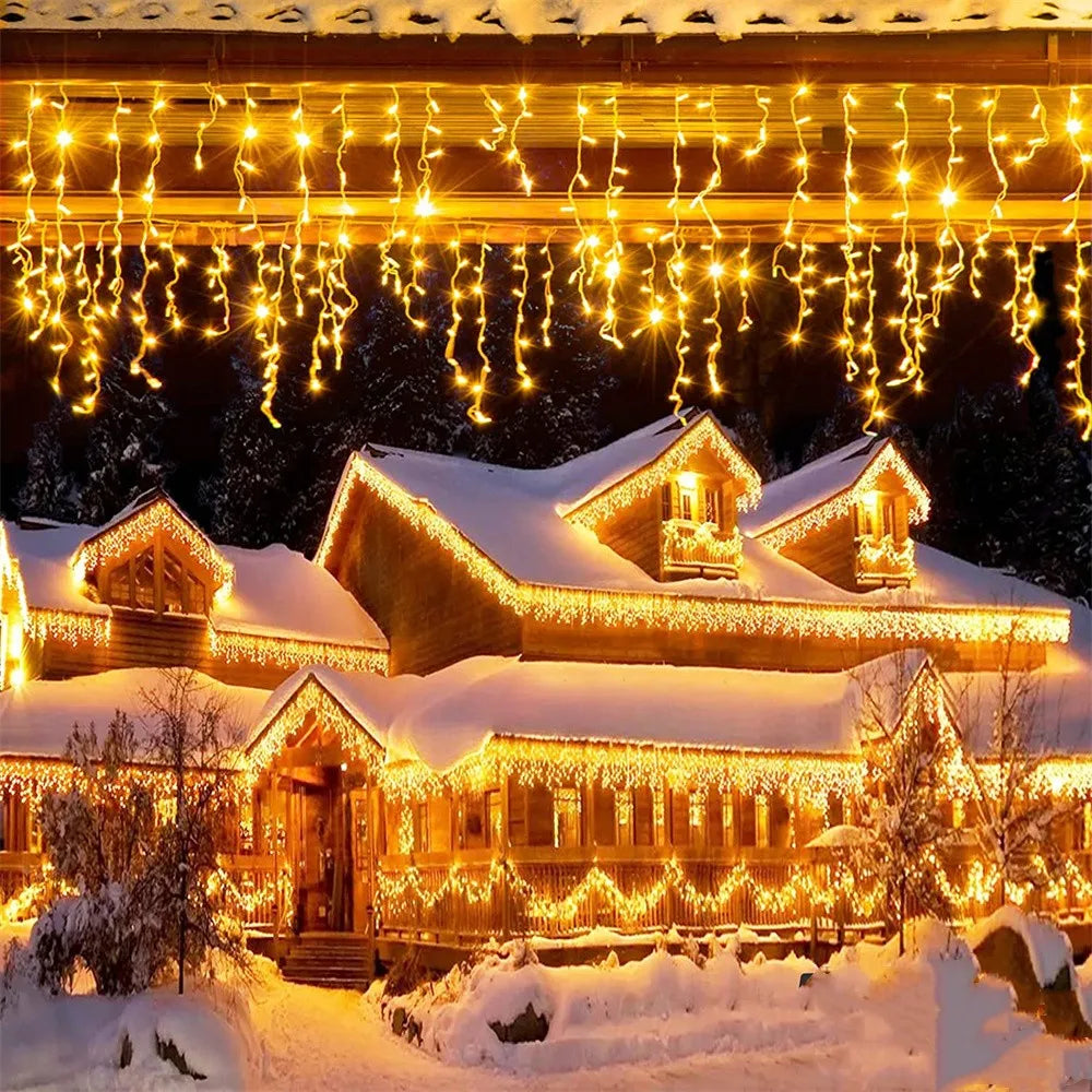 Warm yellow string lights drape over a snowy roof and house facade in a festive outdoor Christmas display.