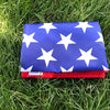 A folded American flag with white stars on a blue field lying on green grass.