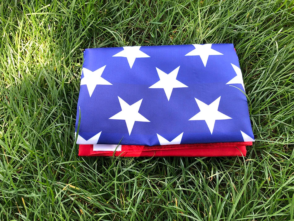 A folded American flag with white stars on a blue field lying on green grass.