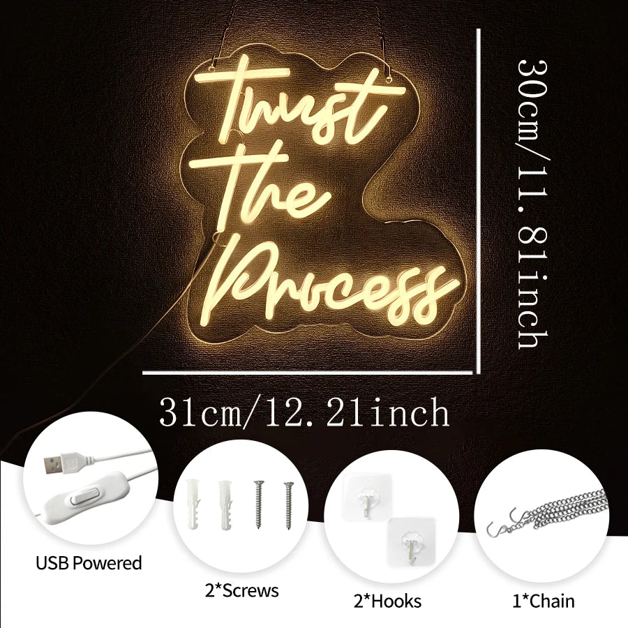 A glowing neon sign shaped like a cloud with the text Trust The Process mounted on a dark background.