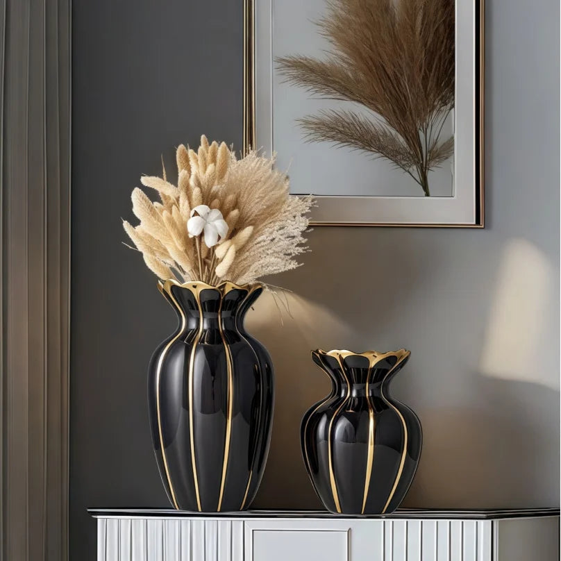 A black gold-plated ceramic flower vase holding dried beige grasses on a gray wall.