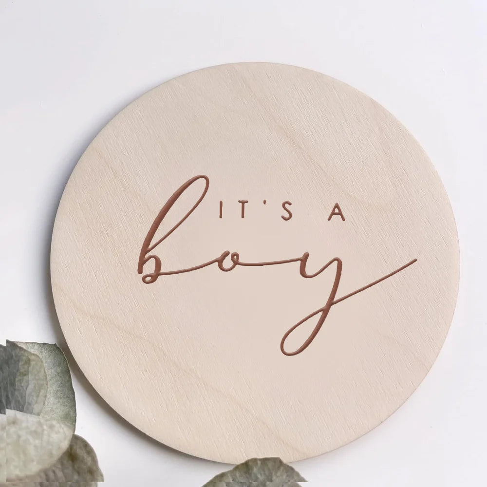 A round, light wood plaque with the script text It's a boy engraved on it.