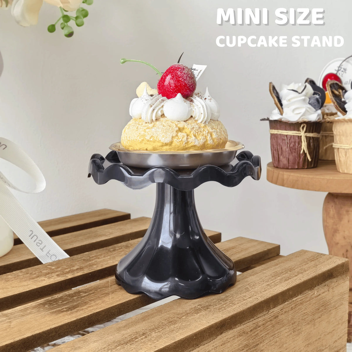 A mini size cupcake stand displaying a single decorated cupcake with cream and a red berry on a wooden surface.