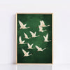 A framed canvas wall art featuring several white cranes in flight against a dark green background.