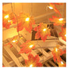 An autumn leaf garland with LED lights is displayed on a white wooden surface.