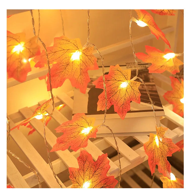 An autumn leaf garland with LED lights is displayed on a white wooden surface.