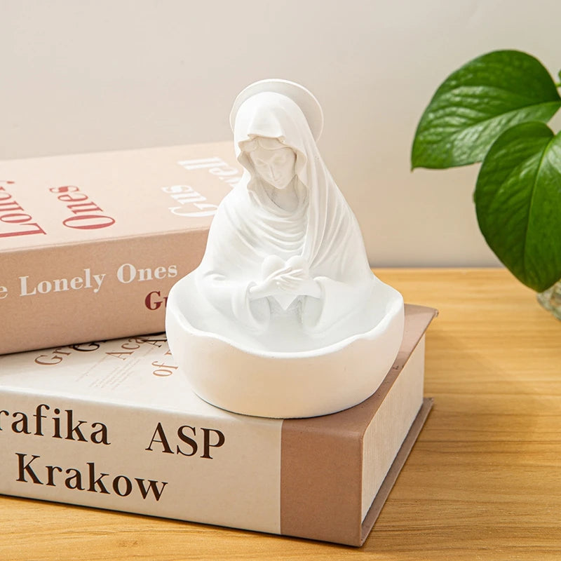 White resin statue of the Virgin Mary with a halo, placed on top of a book.