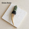 A green stone scepter wand with a wooden tip and black cord wrapped handle displayed on a white square surface.