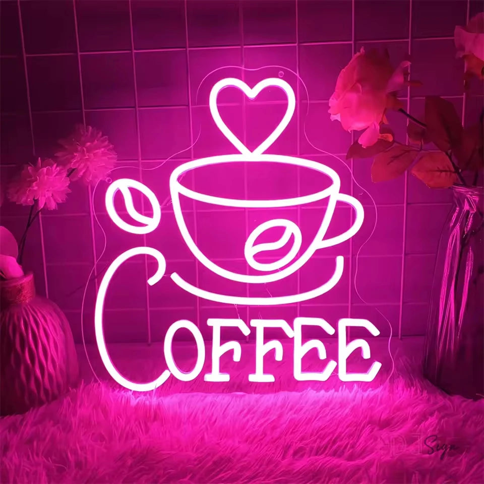 A neon LED wall sign shaped like a coffee cup and the word COFFEE glowing bright pink against a dark background.