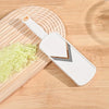 A white manual cabbage shredder with stainless steel blades resting on a wooden cutting board.