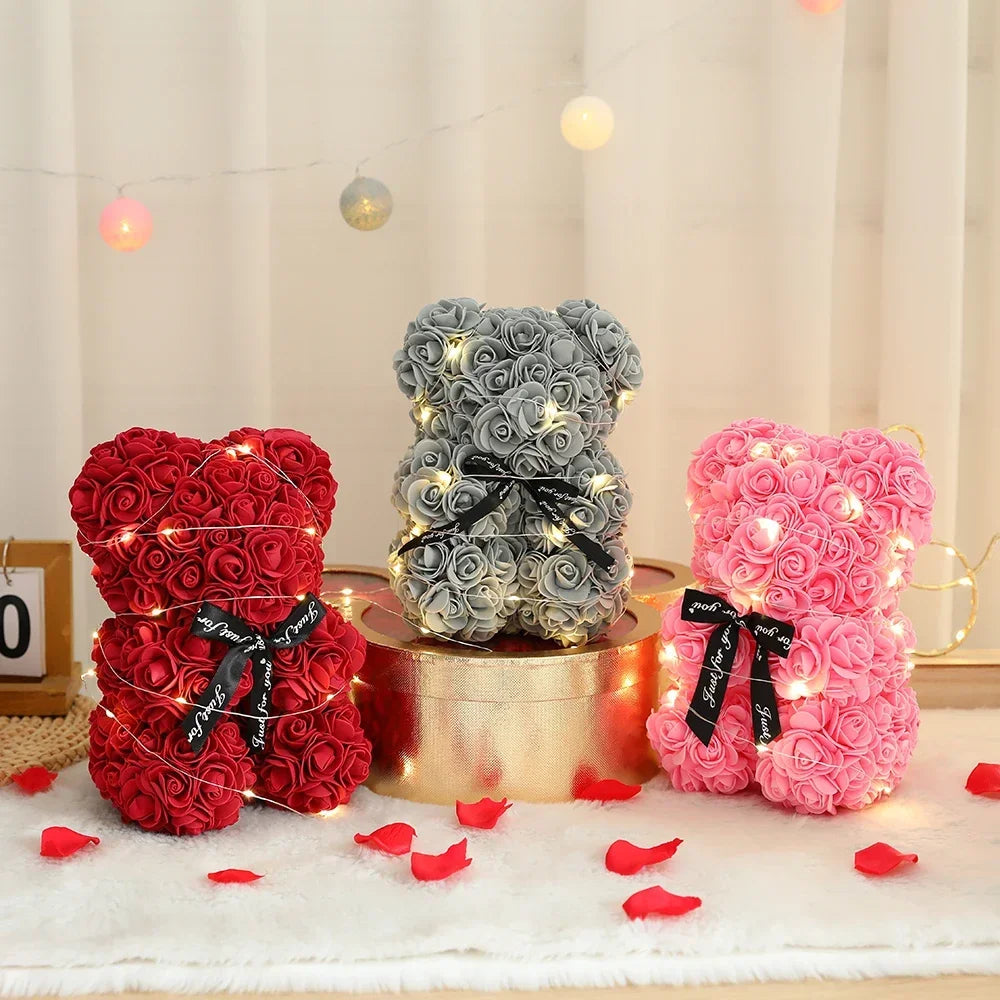 Three artificial rose teddy bears in red, gray, and pink are displayed on a white surface.