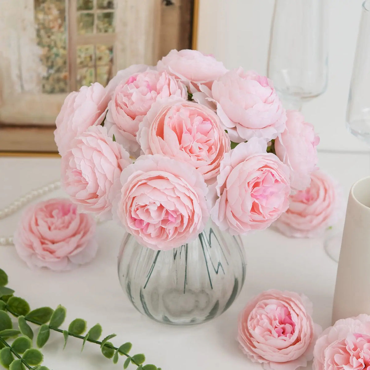 A bouquet of pink silk peony artificial flowers in a glass vase on a white surface.