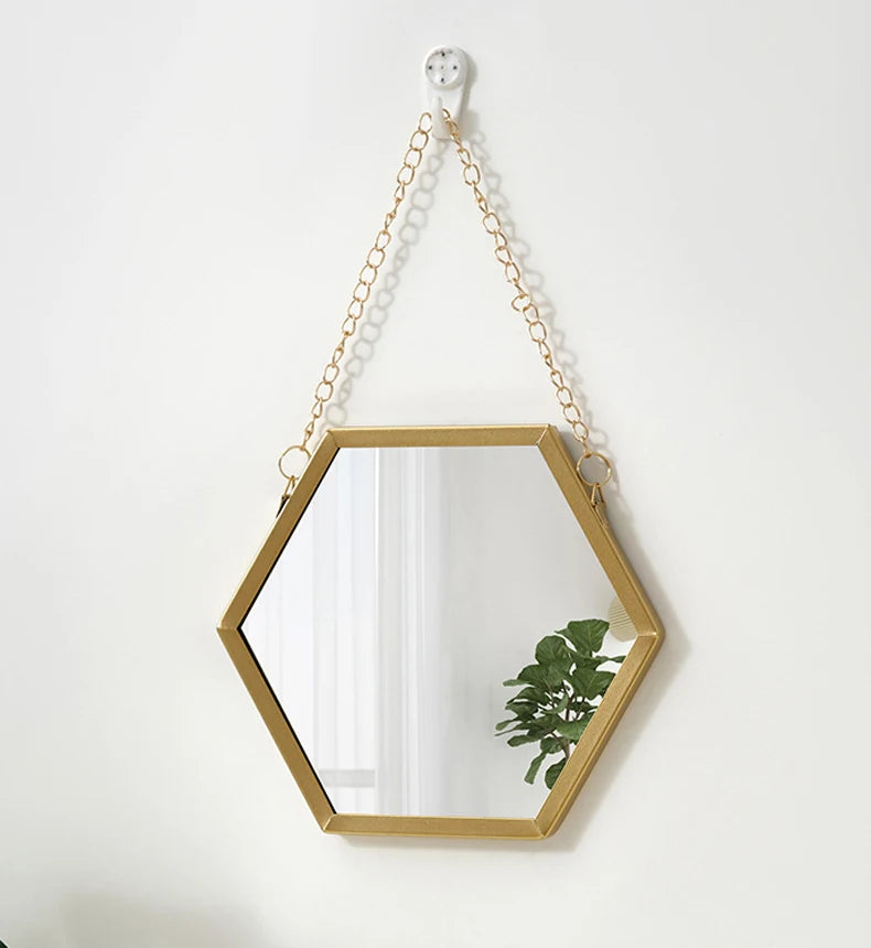 A gold-framed hexagon wall mirror hanging by a chain, with a small green plant visible inside.
