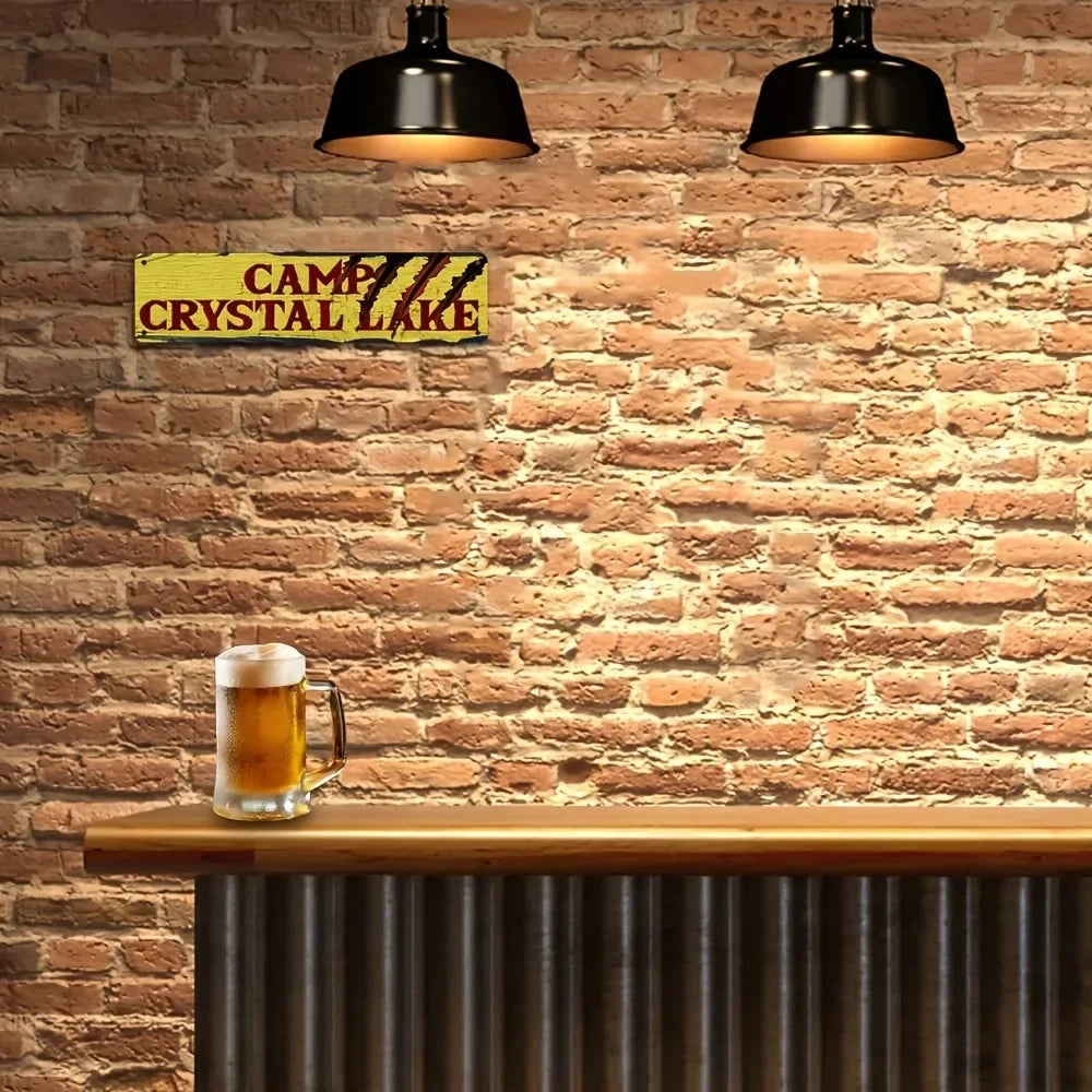 A vintage metal wall sign with yellow lettering reading Camp Crystal Lake mounted on a brick wall above a wooden bar.